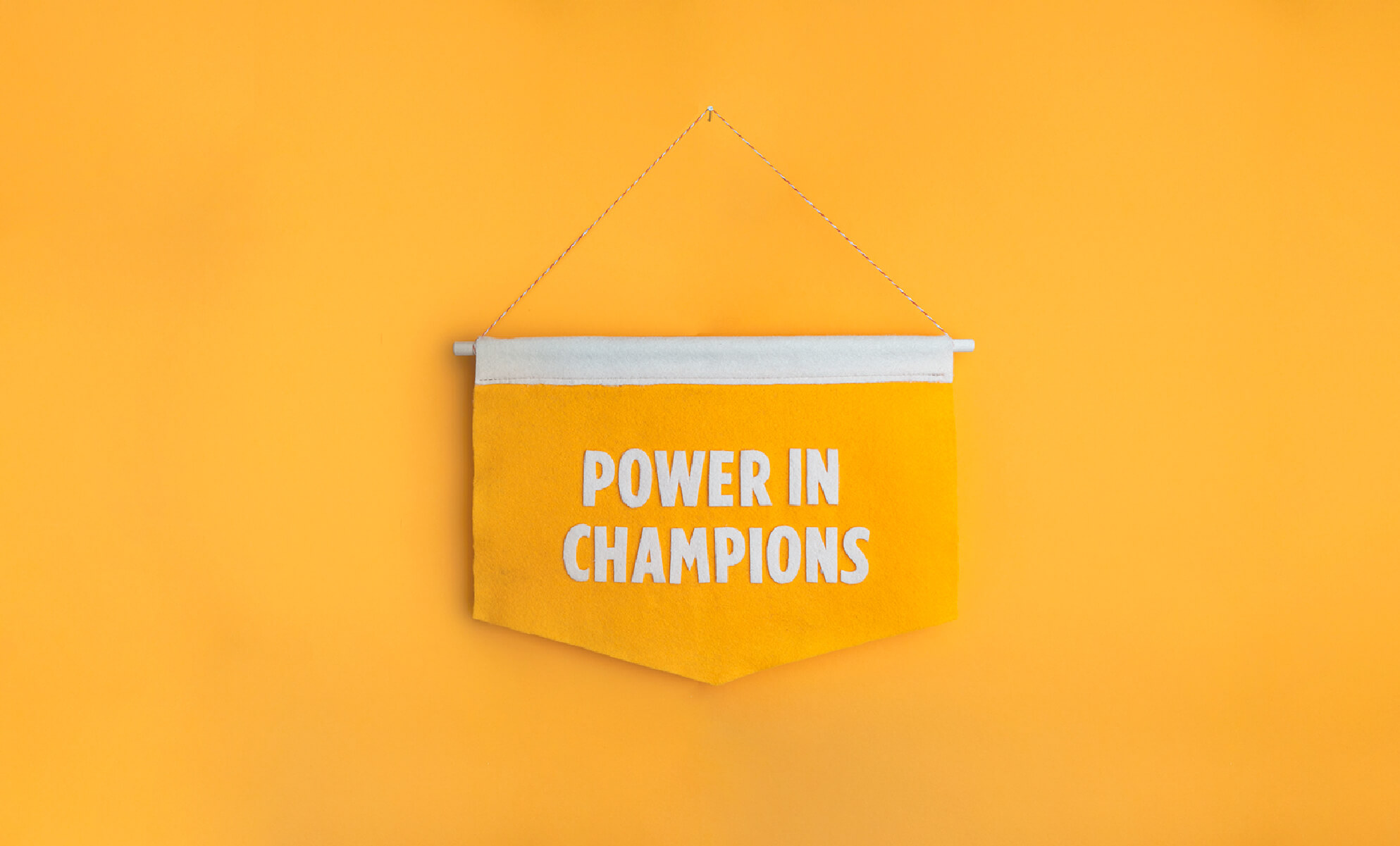 Yellow felt banner with white felt text, "Power in champions," against a yellow wall; image by BrainStorm, Inc. 2020@2x-100