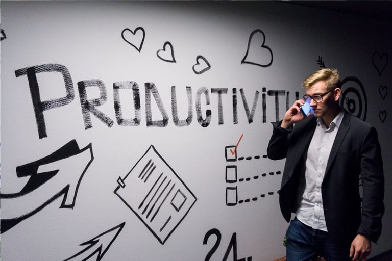 Andreas Klassen for Unpslash: image of man on mobile phone next to a large whiteboard listing the word "Productivity"