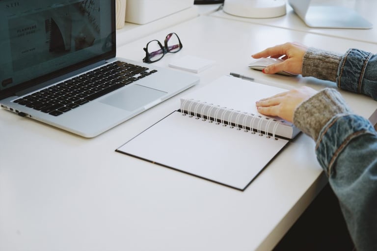 For a blog post on Remote Work: Photo of woman's hands next to a blank notebook, eyeglasses, and an open laptop. Image source: STIL via Unsplash