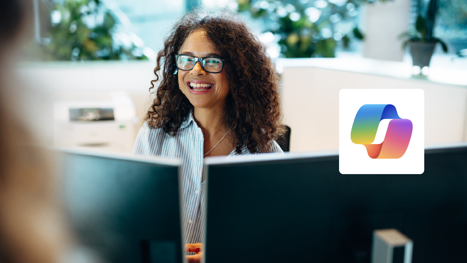 A woman sits in front of a computer, smiling, with the Microsoft 365 Copilot logo to her right.